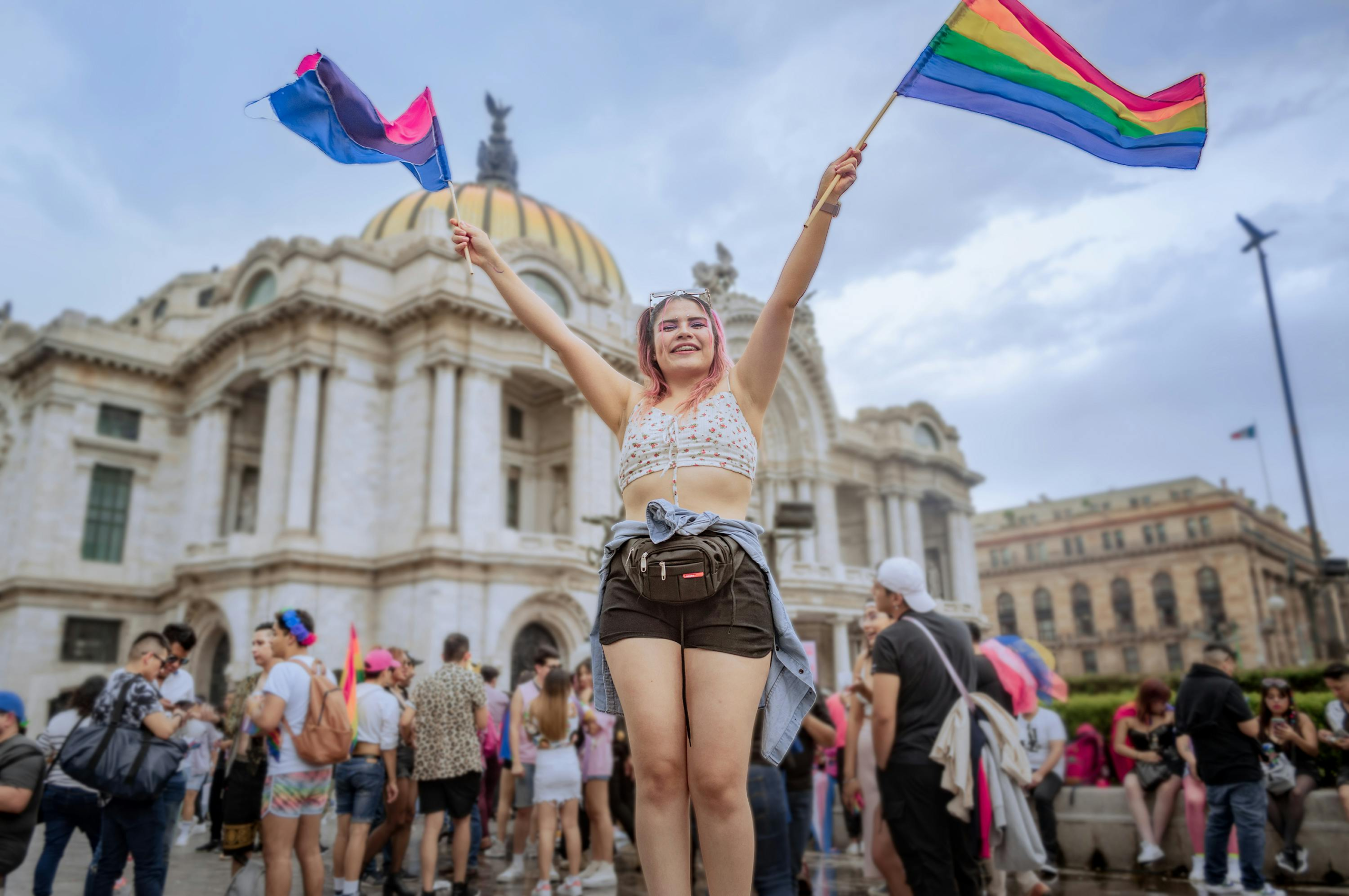A woman waves her arms holding the gay and bisexual flags at a pride parade.