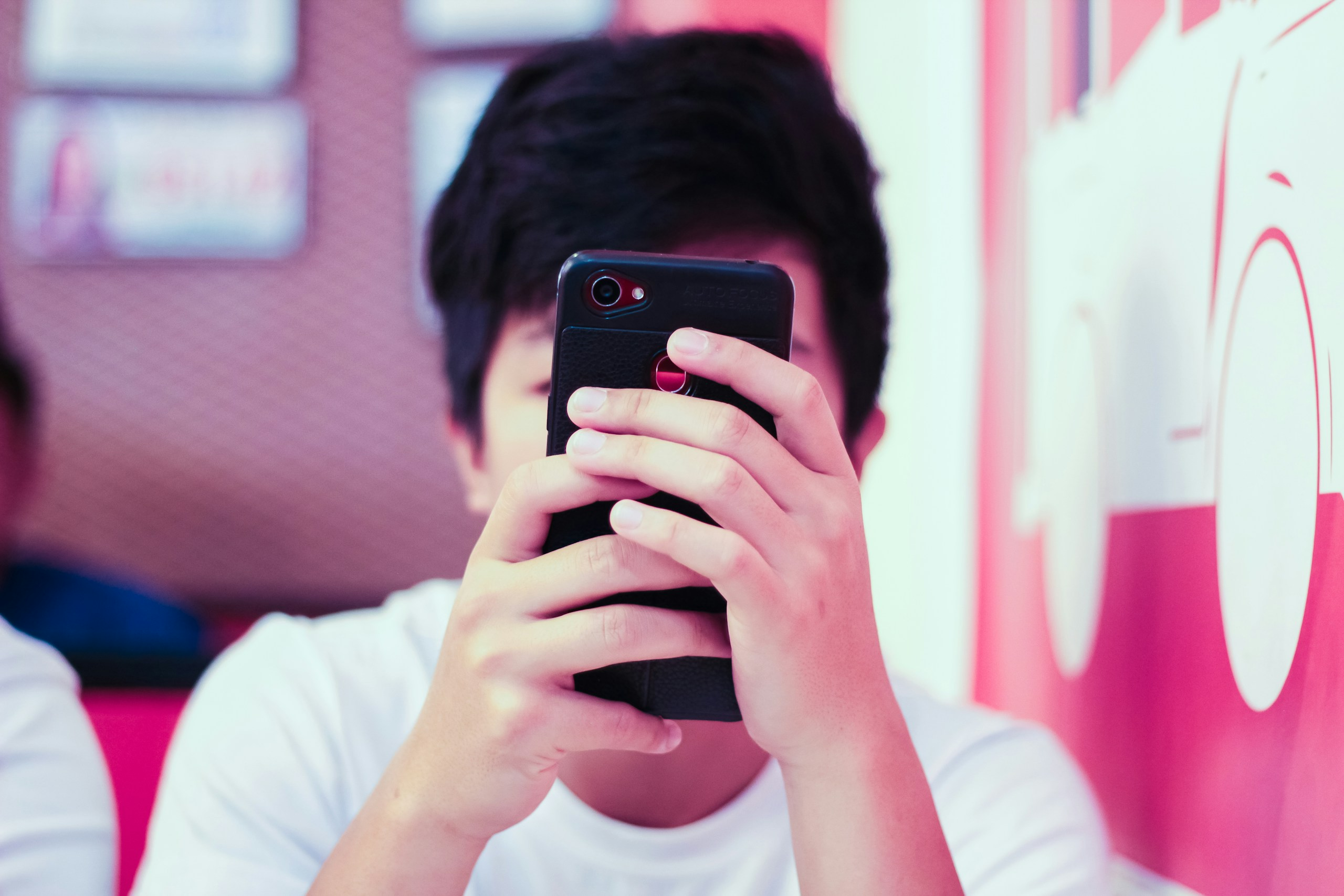 A man in a white t-shirt covers his face with his iPhone as he uses it.