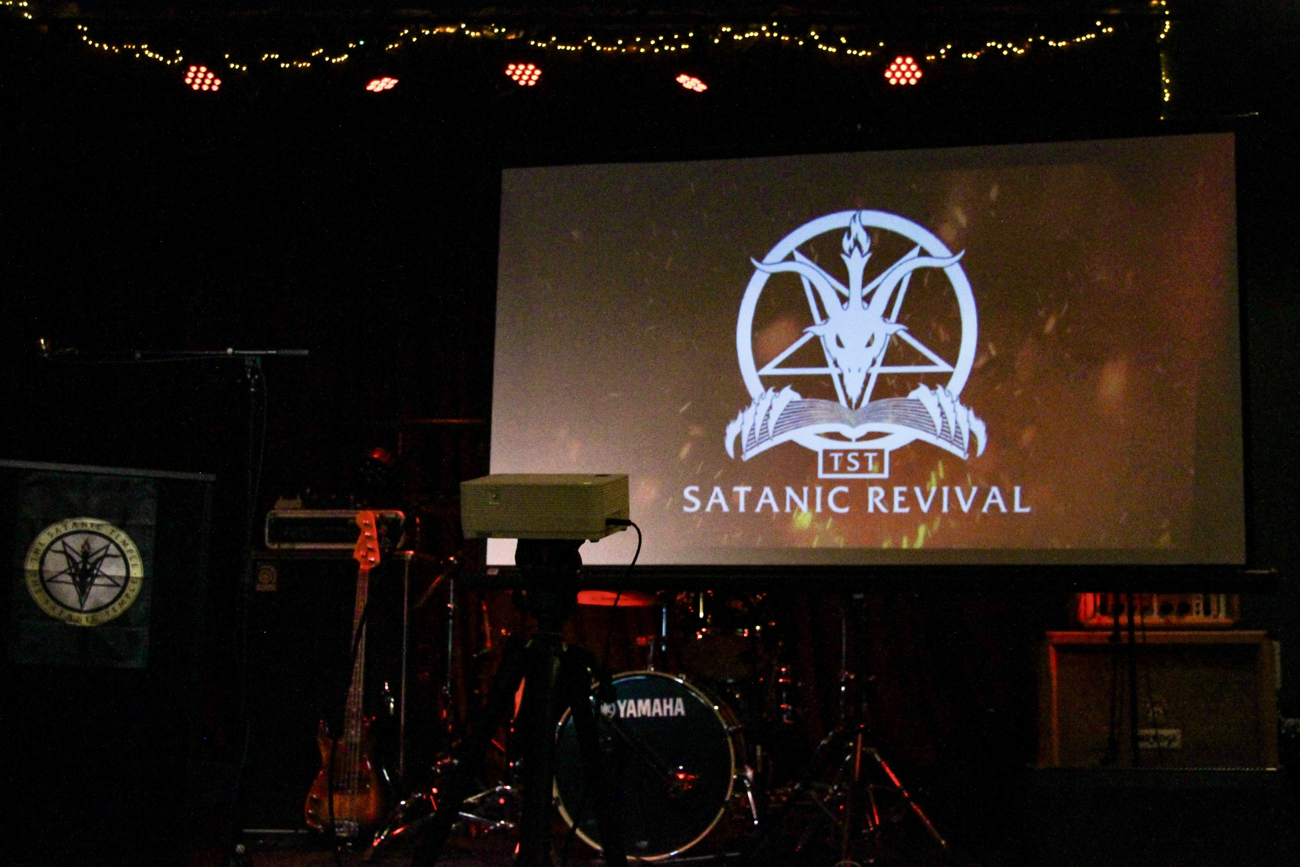 The stage during TST's Satanic Revival event, with a drum set and their logo on display.