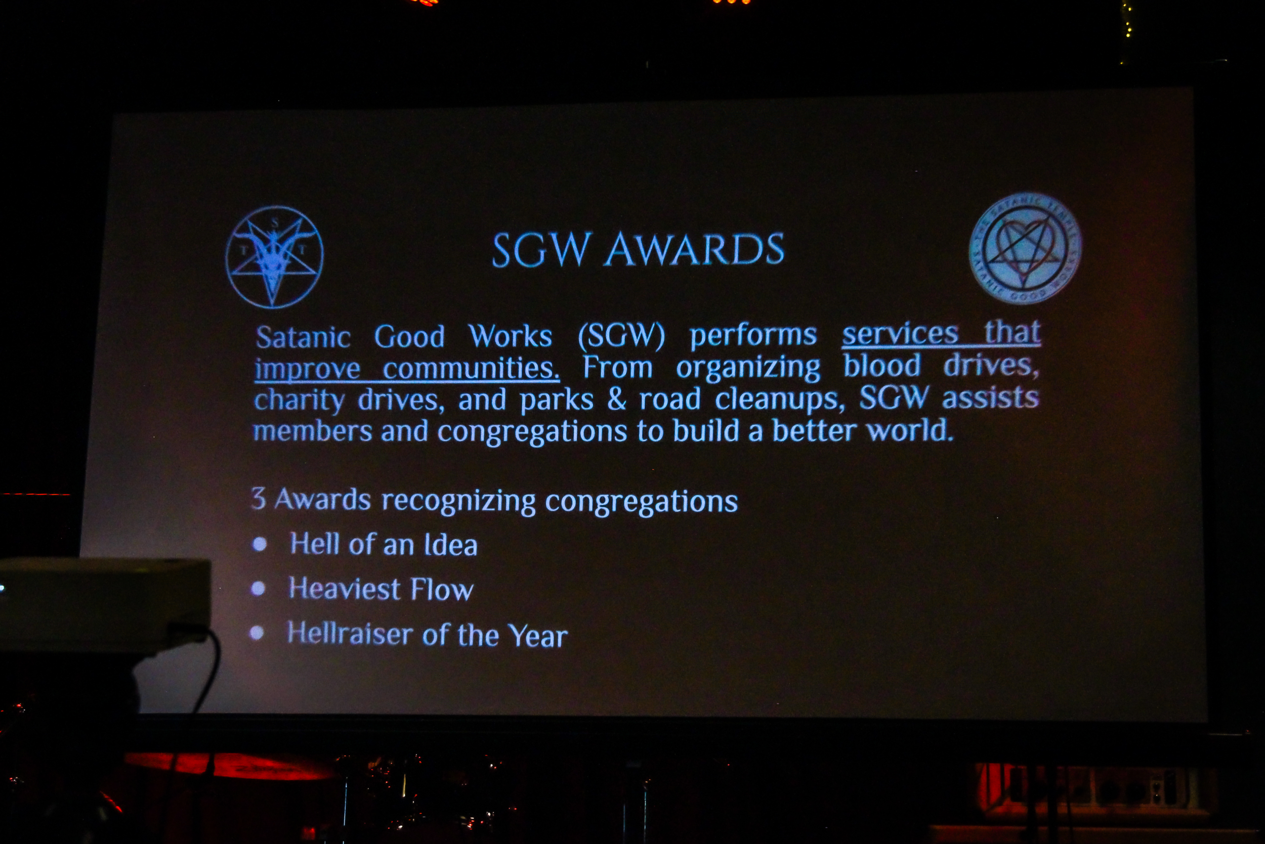 A slideshow explaining the award categories on a projector onstage during the SGW Awards portion of TST's Satanic Revival event.