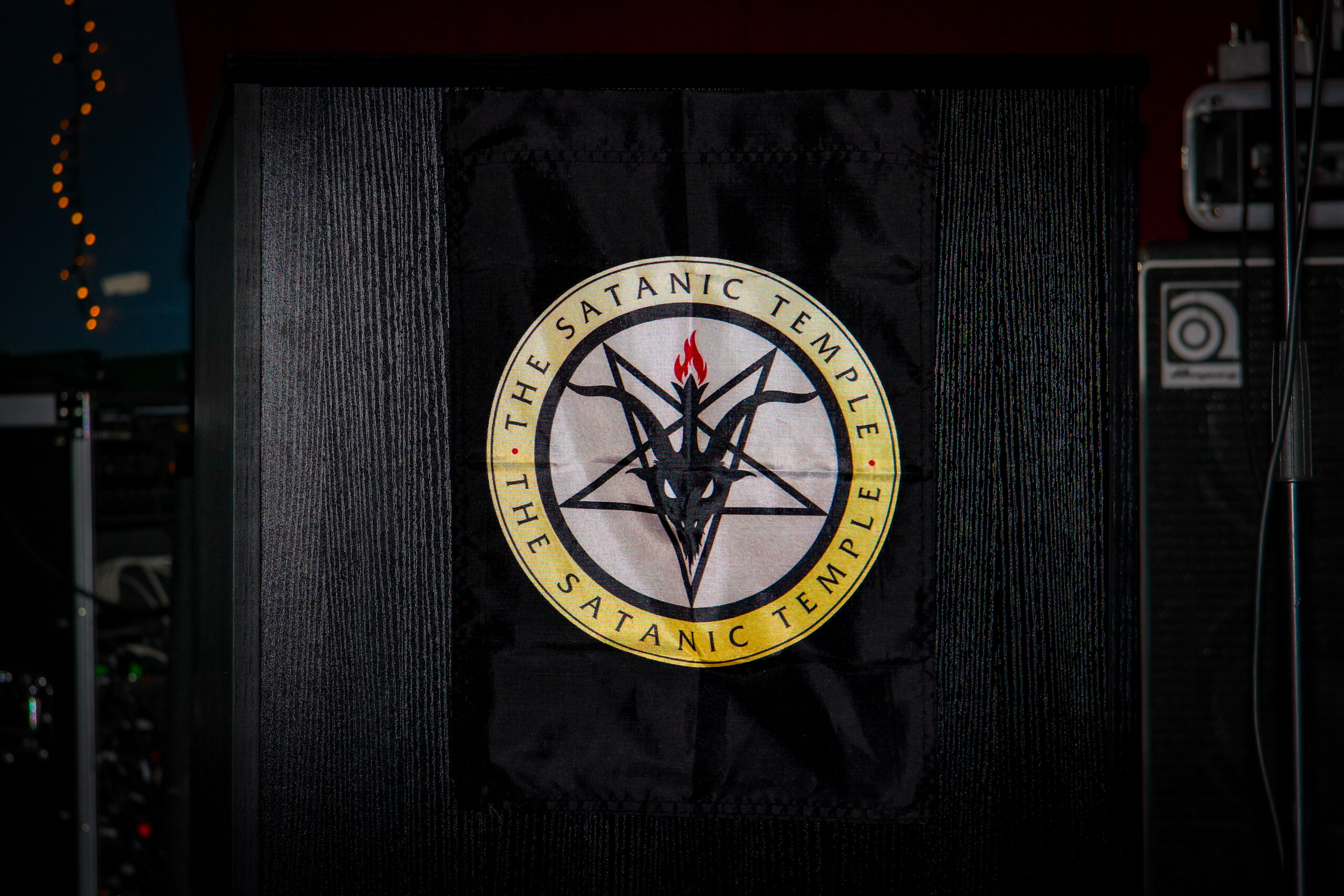 A close up of a podium with TST's logo draped over it onstage at their Satanic Revival event.
