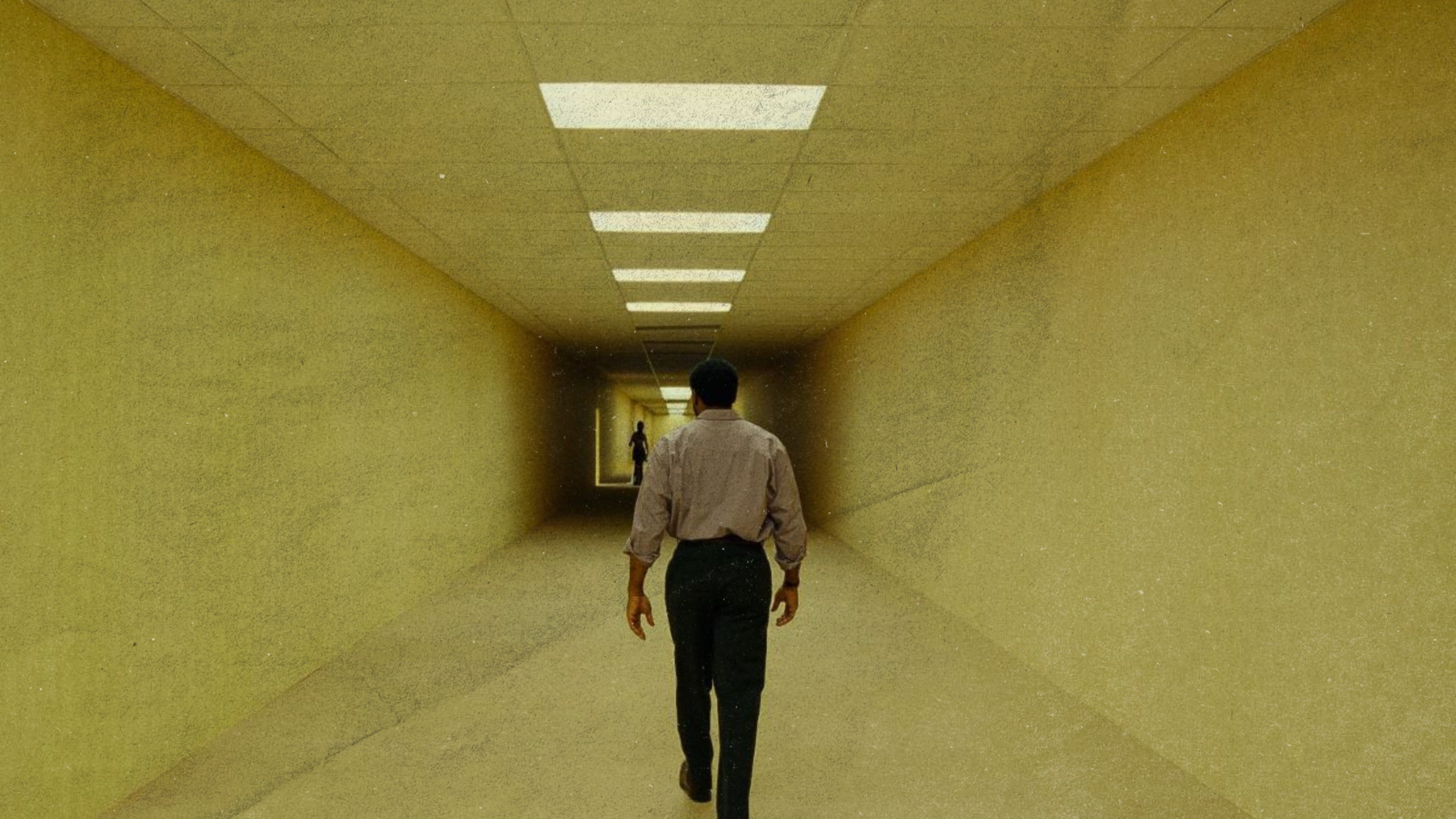 A man walks down one of the halls in the Backrooms. The hall is dark and unsettling, and there's a figure at the end in shadows.